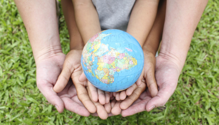 a toy globe in a child's hands, being held by an adult's hands.